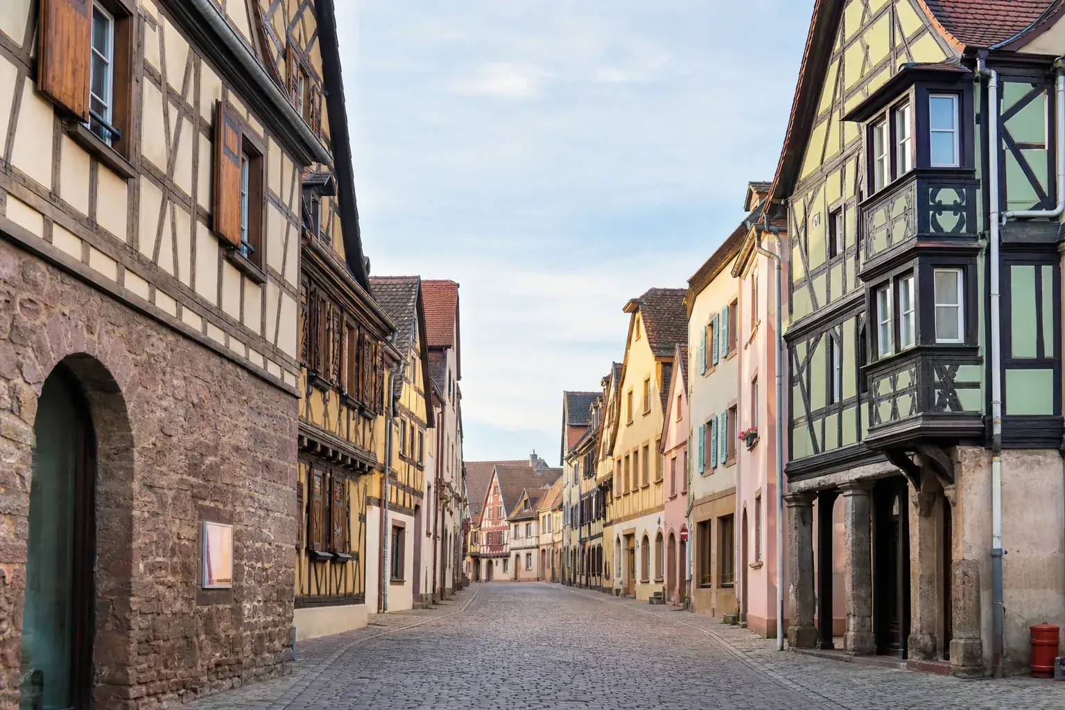 Rue d’un centre-bourg alsacien bordée de maisons à colombages aux façades colorées, ciel dégagé